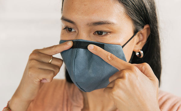 Person wearing the V5 Mask, Pacific Blue, size Small/Medium. Adjusting the conforming nose piece.